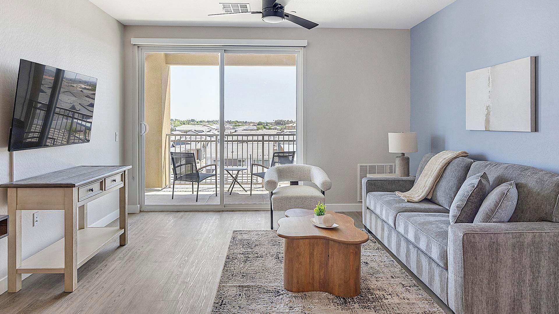 A modern living room with a sofa, coffee table, TV, and a balcony with chairs.