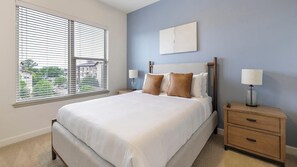 A bedroom with a bed, bedside tables, a nightstand, a lamp, and a window with blinds. - Landing | Stunning 1BD, Gym, Game Room (Fort Worth)