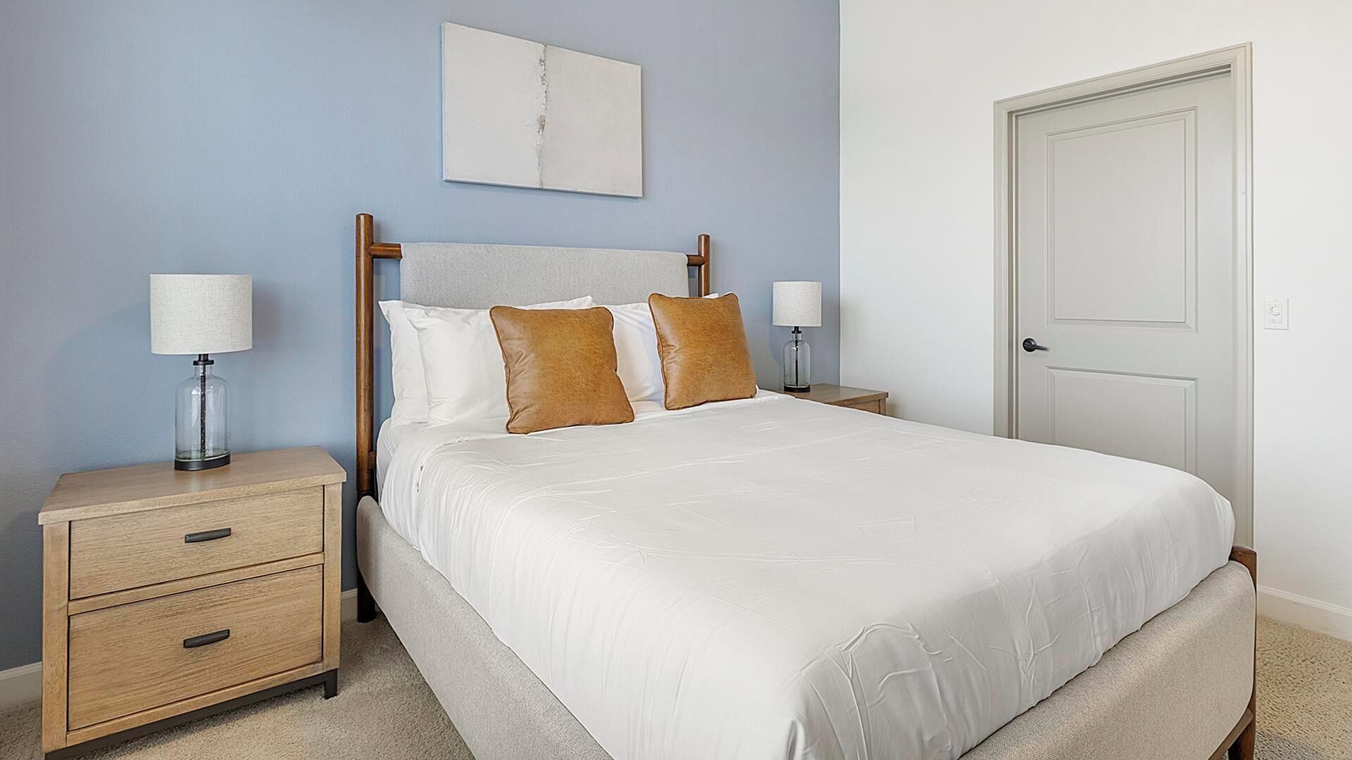 A bedroom with a bed, two bedside tables, a nightstand, a door, and a wall-mounted artwork.