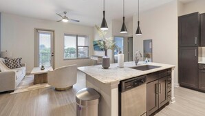 A modern kitchen with a central island, dark cabinetry, and pendant lighting. - Landing | Modern 1BD, Gym, Game Room (Fort Worth)