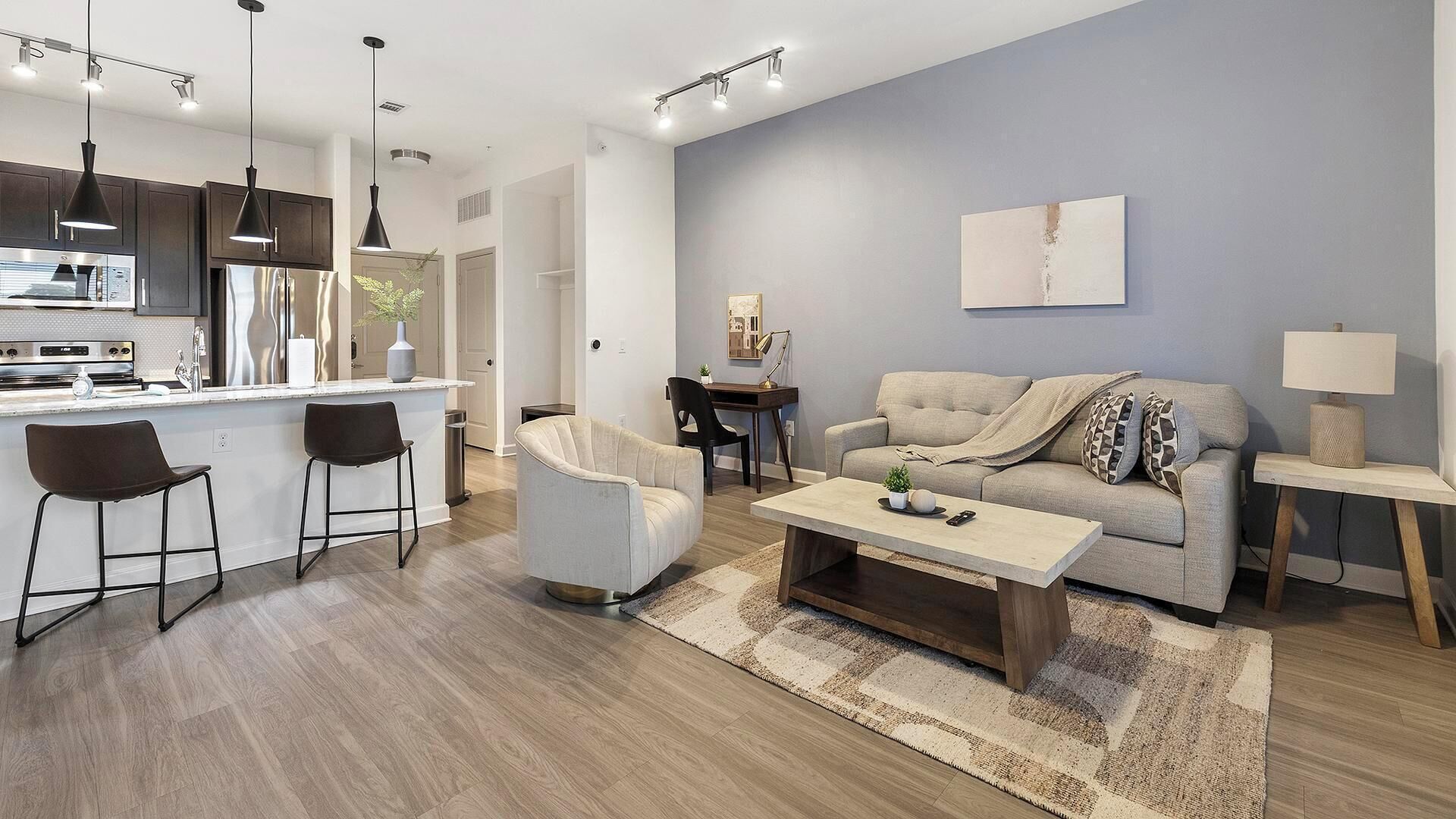 A modern living room with a sofa, coffee table, and chairs. There is a kitchen area with a refrigerator and stove.