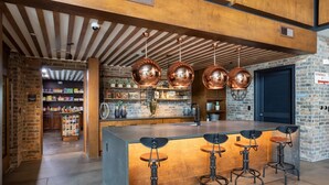 A modern kitchen with a central island, bar stools, hanging copper pendant lights, and a brick wall. - Landing | Modern 1BD, Gym, Game Room (Fort Worth)