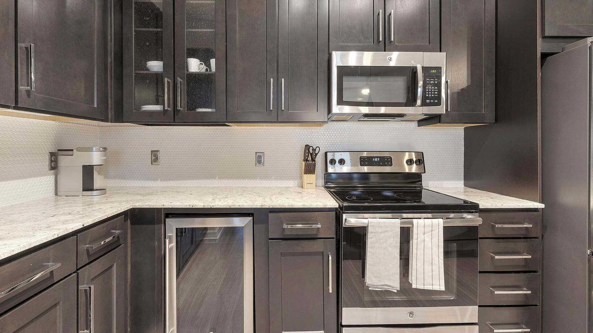 A modern kitchen with dark cabinetry, stainless steel appliances, and a white countertop.