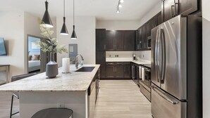 A modern kitchen with dark cabinets, stainless steel appliances, and pendant lighting. - Landing | Modern 1BD, Gym, Game Room (Fort Worth)