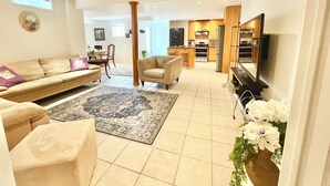 Una sala de estar con un sofá, sillones, una mesa de centro y una alfombra. Hay una zona de cocina con armarios y electrodomésticos.