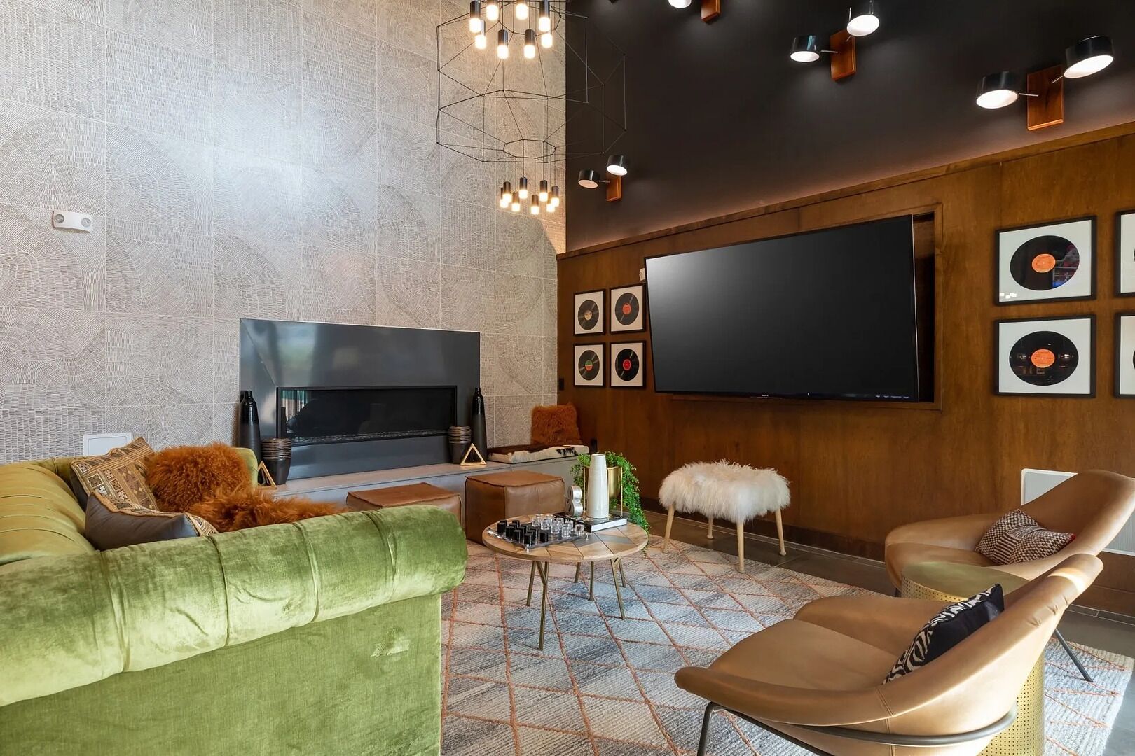A modern living room with a large flat-screen TV, a green sofa, a brown leather chair, and a patterned rug.