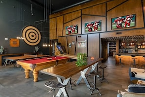 Ein Billardtisch, eine Dartscheibe und ein Barbereich mit Hockern und einer Theke.