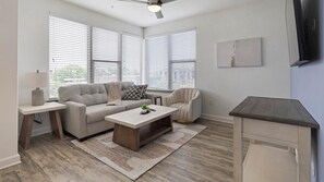 A living room with a sofa, armchair, coffee table, and a TV on a stand. - Landing | Chic 1BD, Gym, Game Room (Fort Worth)