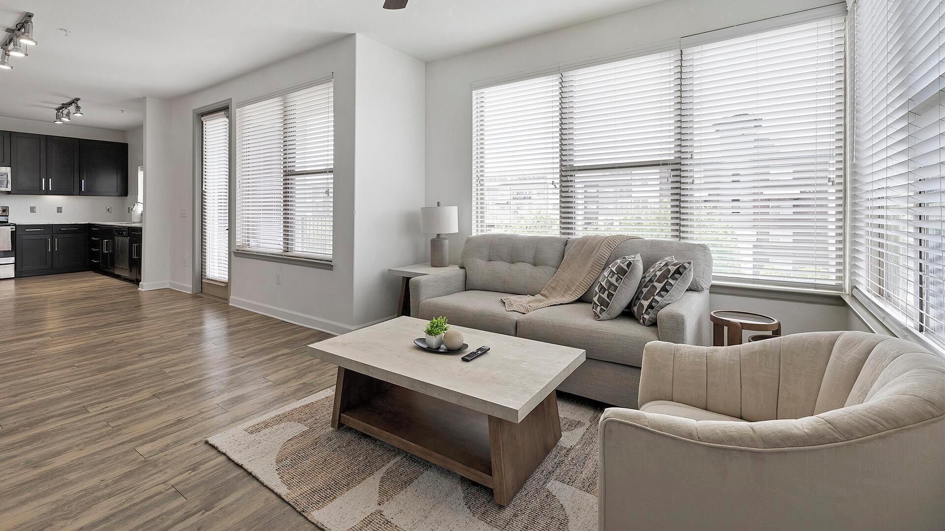 Un salon moderne comprenant un canapé, un fauteuil, une table basse et de grandes fenêtres équipées de stores.