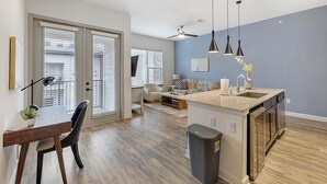 Una cocina moderna con una isla central, un comedor con mesa y sillas, y una sala de estar con sofá y televisor.
