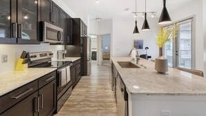 Una cocina moderna con armarios oscuros, una isla grande, electrodomésticos de acero inoxidable e iluminación colgante.