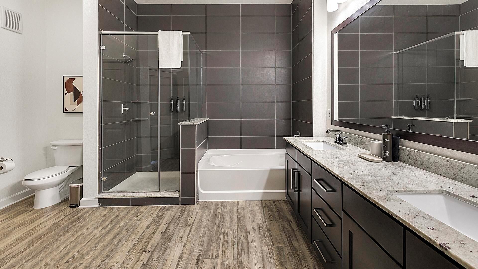 A modern bathroom with a glass shower enclosure, a bathtub, a toilet, and a large mirror.