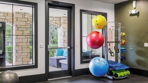 Ein Fitnessraum mit Übungsbällen, einem an der Wand befestigten Widerstandsbandhalter und Blick durch Glastüren nach draußen.