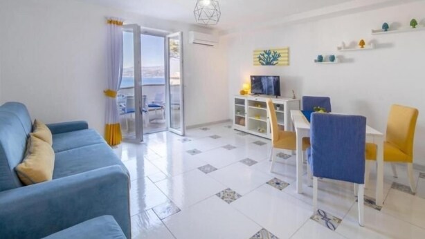 A living room with a sofa, a dining table with chairs, a TV, and a balcony with a view. - Casa Floriana Seaview - Panoramic Terrace in Capri (Capri)