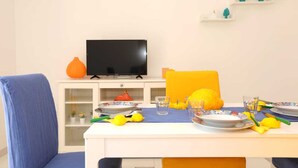 A dining area with a table set for two, a television on a cabinet, and decorative items on shelves. - Casa Floriana Seaview - Panoramic Terrace in Capri (Capri)