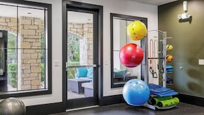 Ein Fitnessraum mit Übungsbällen, einem an der Wand befestigten Widerstandsbandhalter und Blick durch Glastüren nach draußen.