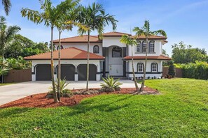A two-story house with a red-tiled roof, a garage, and a well-maintained lawn with palm trees. - Glam Manor by Glam Homes (Sunrise)