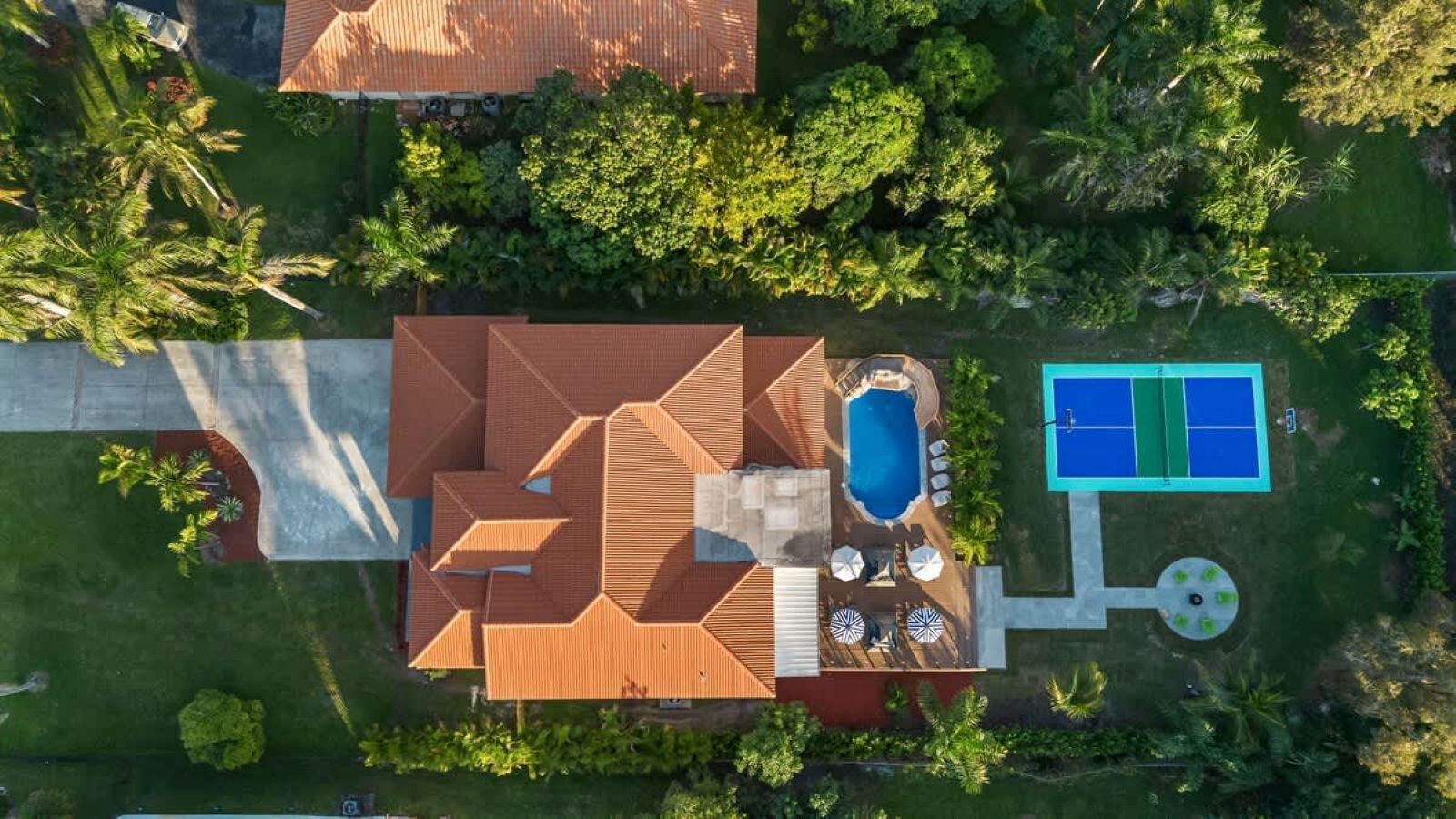 An aerial view of a house with a swimming pool, a patio area, and lush greenery.