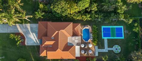 An aerial view of a house with a swimming pool, a patio area, and lush greenery.