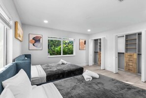 A modern bedroom with a large bed, a blue sofa, and a walk-in closet with wooden drawers. - Glam Manor by Glam Homes (Sunrise)