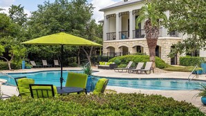 Un área de piscina con sillones de descanso, una mesa y una sombrilla grande.