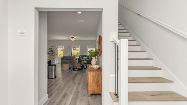 A staircase with wooden steps and white railings leading to a living area with a sofa, a coffee table, and a ceiling fan. - Fall Savings - House w/ Pool, indoor games & only 5 miles to Navarre Beach (Navarre)