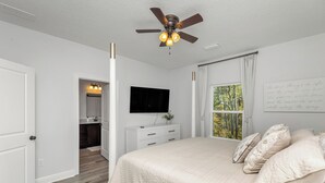 A bedroom with a bed, a ceiling fan, a TV, and a window with curtains. - Fall Savings - House w/ Pool, indoor games & only 5 miles to Navarre Beach (Navarre)