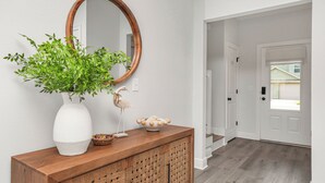 A hallway with a wooden console table, a white vase with green foliage, a decorative bird sculpture, and a round mirror. - Fall Savings - House w/ Pool, indoor games & only 5 miles to Navarre Beach (Navarre)