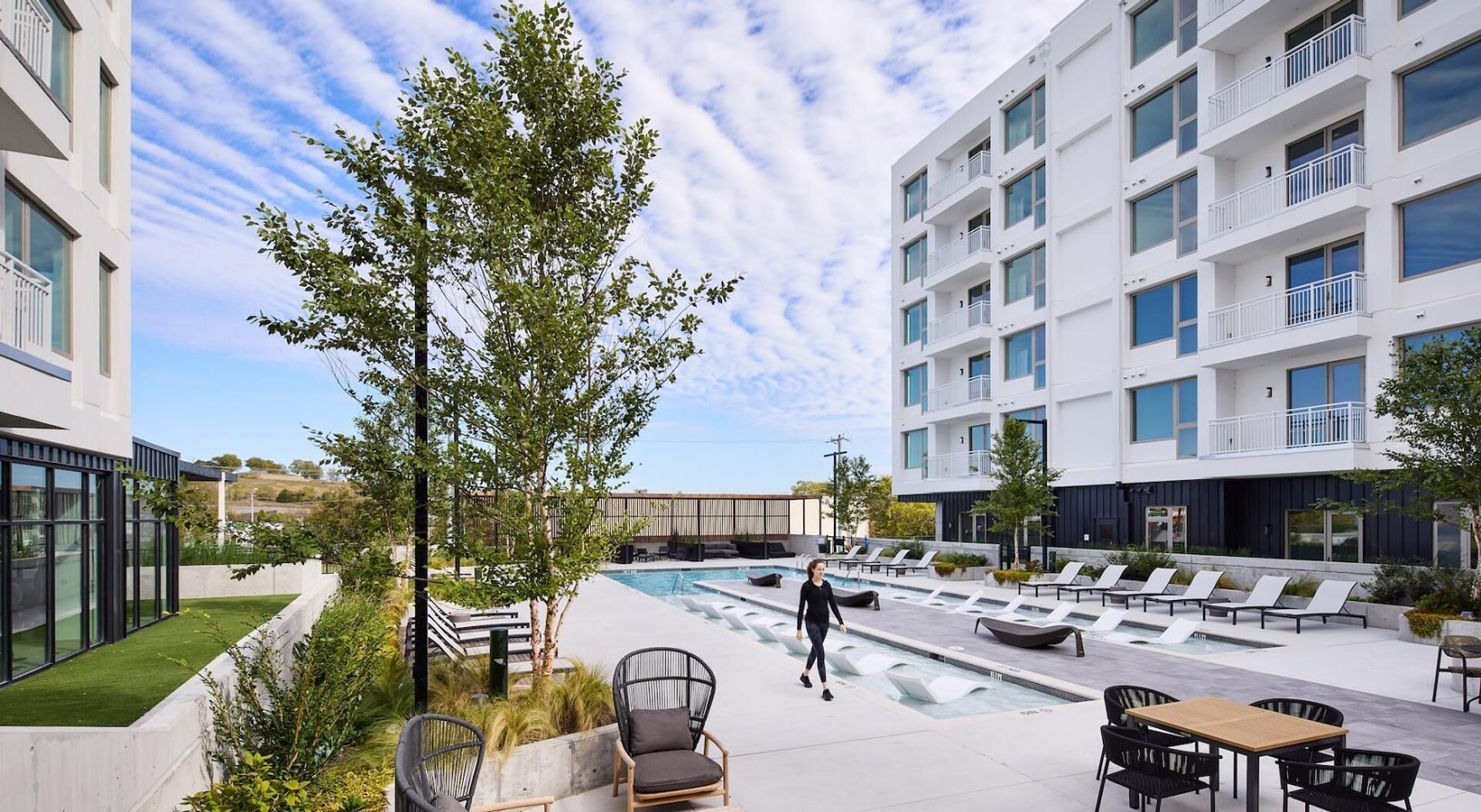 A modern outdoor pool area with lounge chairs, a wooden table, and a walking path.