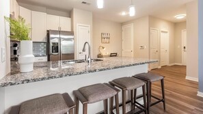A modern kitchen with a granite countertop, stainless steel appliances, and a bar area with stools. - Landing | Modern 2BD, Yoga Studio, Gym (Huntersville)