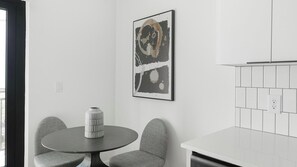 Eine moderne Küche mit weißen Schränken, einem runden Tisch mit zwei Stühlen und einem gerahmten abstrakten Gemälde an der Wand.