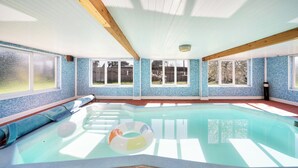 A swimming pool with clear blue tiles, wooden beams, and large windows.