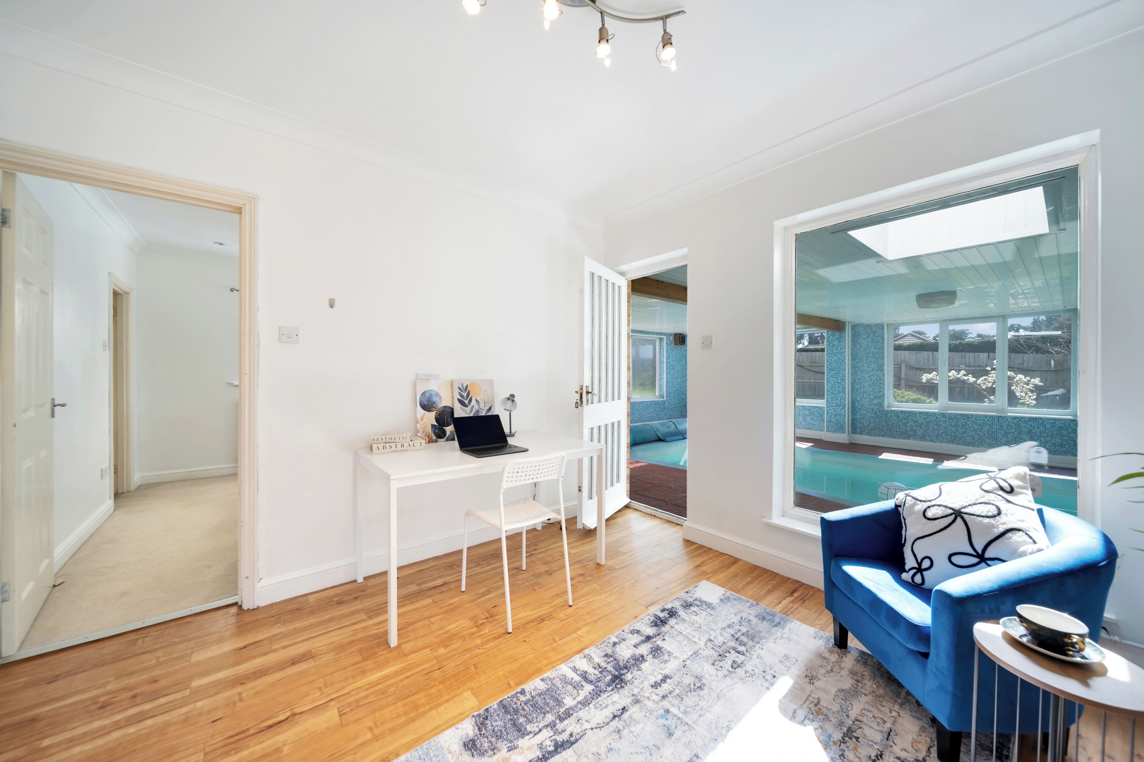 A modern living room with a white desk, a blue sofa, and a view of a swimming pool.