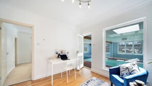 A modern living room with a white desk, a blue sofa, and a view of a swimming pool.