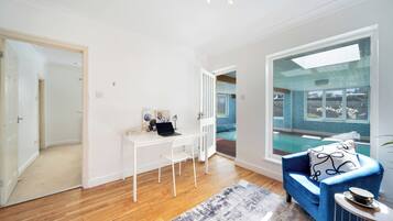 A modern living room with a white desk, a blue sofa, and a view of a swimming pool.