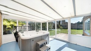 A hot tub in a covered patio area with large windows and a view of the backyard.