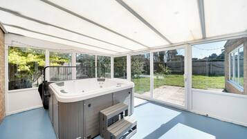 A hot tub in a covered patio area with large windows and a view of the backyard.