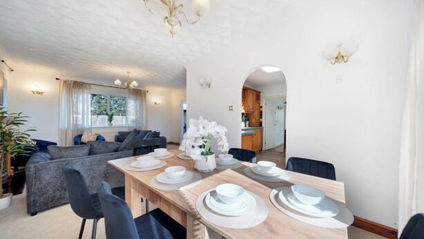 A modern dining area with a wooden table set for four, a sofa, and a view of the kitchen.
