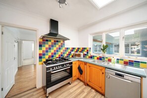 A kitchen with a gas stove, oven, and dishwasher, wooden cabinets, a colorful backsplash, and a window with a view.
