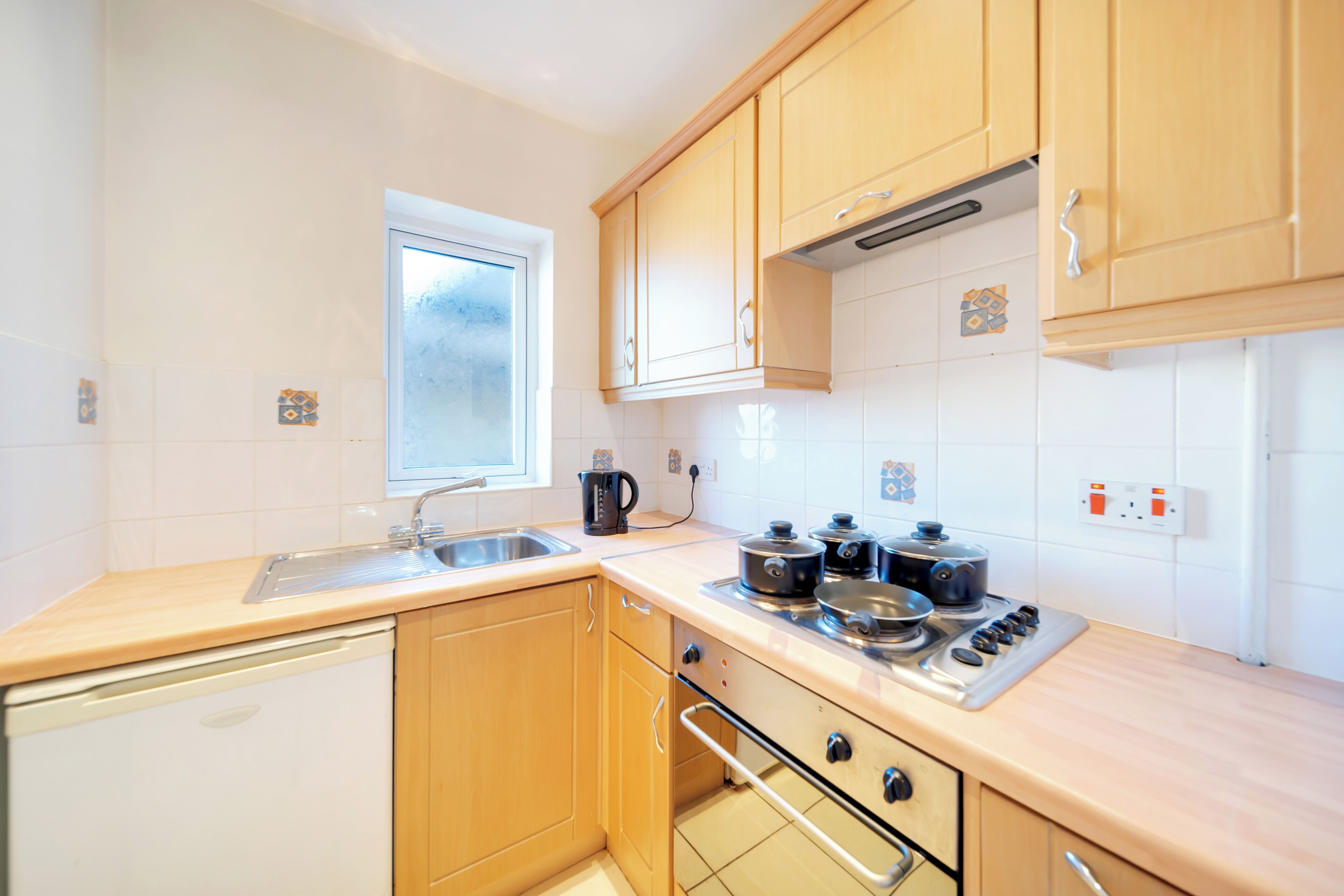 A compact kitchen with wooden cabinets, a built-in oven, a sink, and a window.