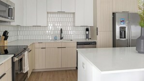 Eine moderne Küche mit weißen Schränken, einem Edelstahl-Kühlschrank, einer Kaffeemaschine und einem Geschirrspüler.