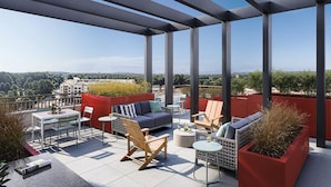 Een terras op het dak met uitzicht over de stad, met een bank, stoelen en een tafel.
