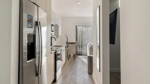 A modern kitchen with stainless steel appliances, a dining area, and a view through a glass door. - Landing | Stunning Studio, Gym, Courtyard (Chapel Hill)