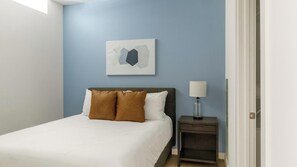 Une chambre à coucher comprenant un lit, une table de chevet, une lampe et une œuvre d’art abstraite accrochée au mur.