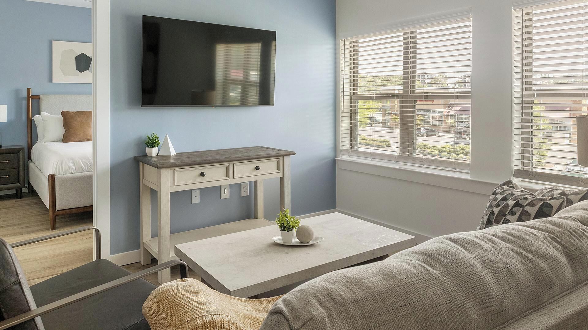 A modern living room with a sofa, a coffee table, a TV, and a window with blinds.