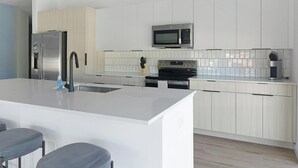 A modern kitchen with a central island, stainless steel appliances, and light wood cabinetry. - Landing | Beautiful 3BD, Gym, Courtyard (Chapel Hill)