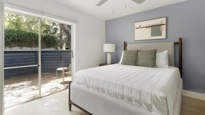 Ein Schlafzimmer mit einem Bett, einem Nachttisch, einer Lampe, einem Deckenventilator und einer Schiebetür zu einem Außenbereich.