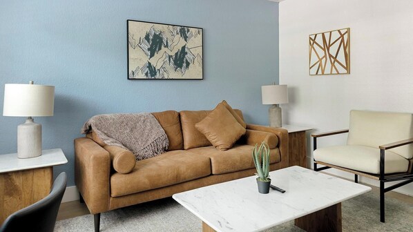 Ein Wohnzimmer mit einem braunen Sofa, einem weißen Couchtisch, einem Sessel und zwei Lampen.