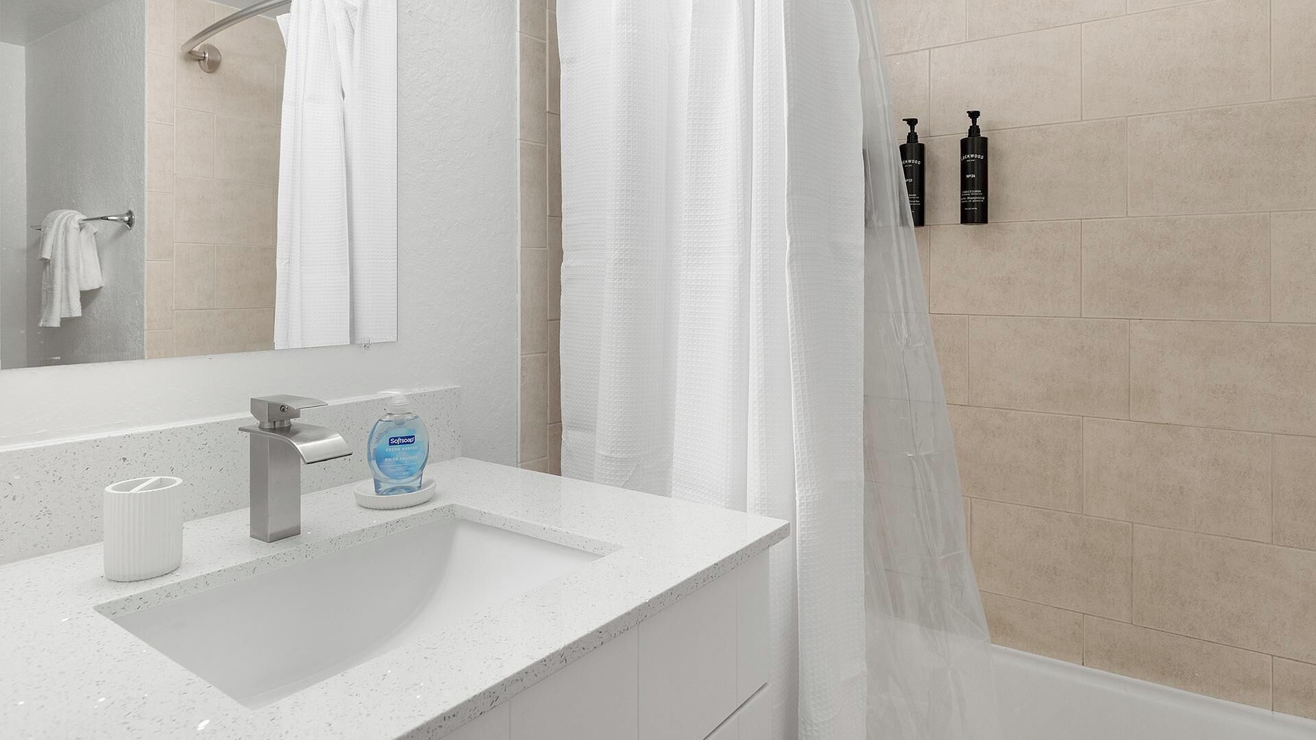 A modern bathroom with a white sink, a mirror, a shower curtain, and toiletries on the wall.