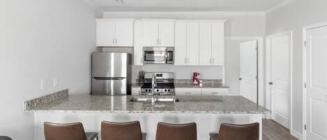 A modern kitchen with white cabinets, stainless steel appliances, granite countertops, and four bar stools.